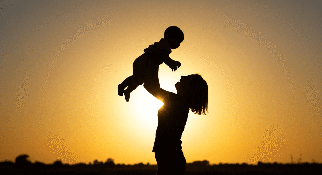 Silueta de madre elevando a su bebé al atardecer junto al mar. Imagen de amor maternal y alegría para celebrar el día de la madre o la familia.
