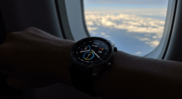 Reloj inteligente Moto 360 en la muñeca de una persona dentro de un avión. Vista de la ventana con el cielo y las nubes. Ideal para blogs de tecnología y viajes.
