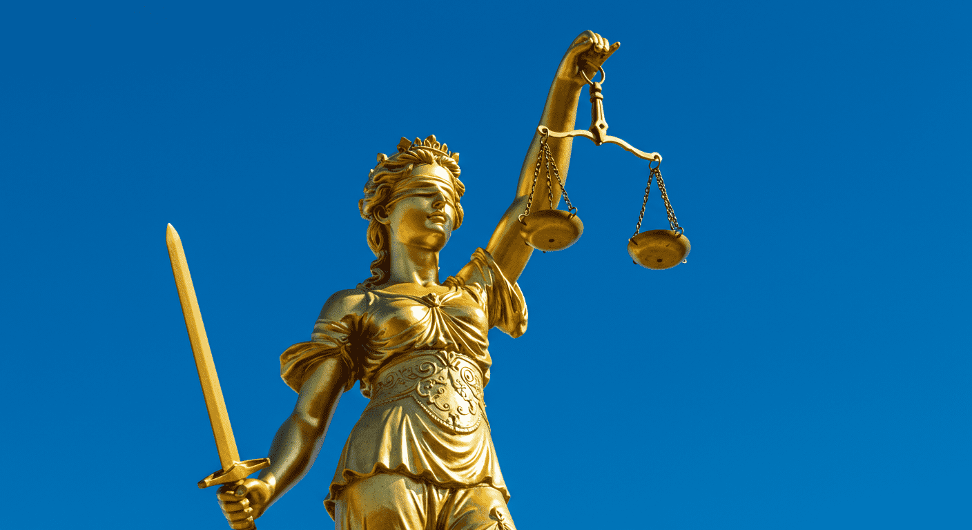 Estatua dorada de la Justicia con balanza y espada sobre cielo azul. Símbolo del derecho y la equidad. Accesible.