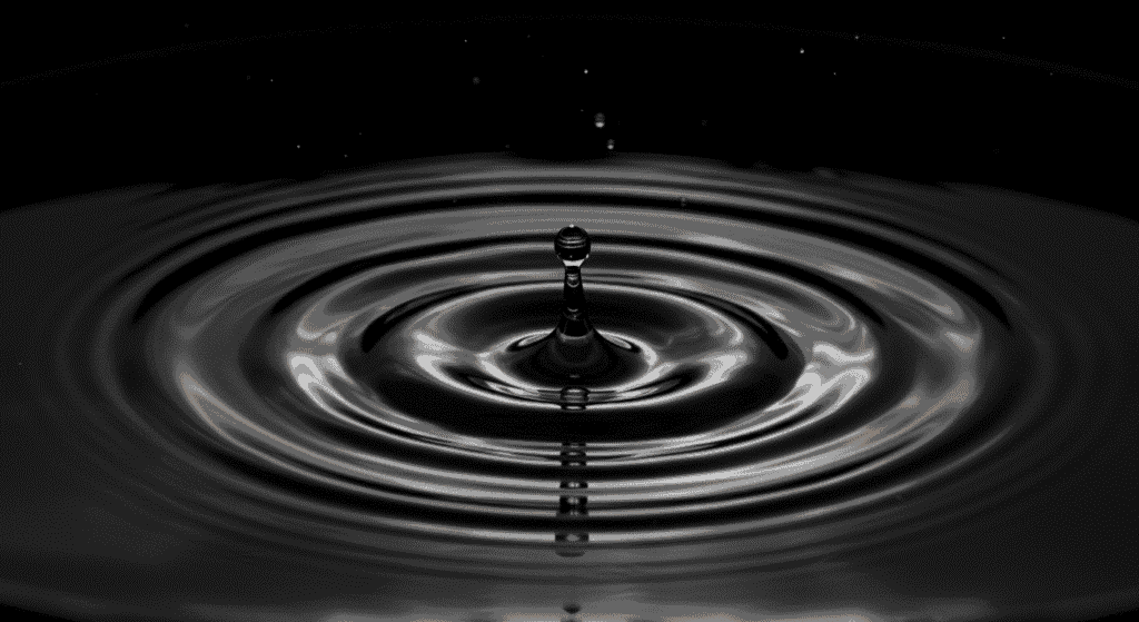 Primer plano de una gota impactando una superficie líquida oscura, generando ondas circulares. Imagen de alta calidad para temas de física, fluidos y fenómenos naturales.

