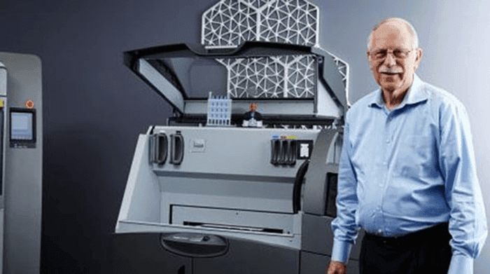 Cómo la Impresión 3D Está Revolucionando la Industria 2 Hombre e impresora 3D: Persona sonriendo junto a impresora tridimensional en entorno industrial. Accesibilidad web y SEO para tecnología, fabricación digital y diseño.