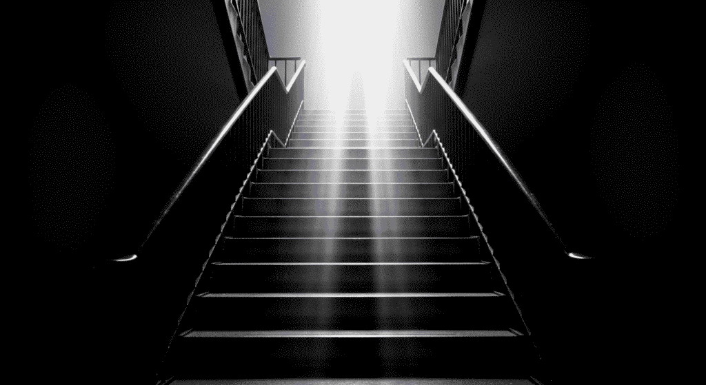 Escalera iluminada con un rayo de luz. Imagen en blanco y negro de una escalera misteriosa. Fotografía de escalera con iluminación dramática.

