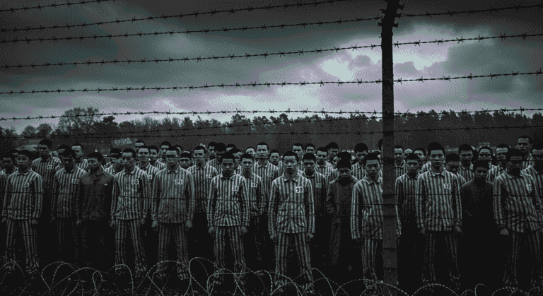 Fotografía en blanco y negro de personas con uniformes a rayas tras alambrada. Imagen impactante de represión y confinamiento. Alambre espino.