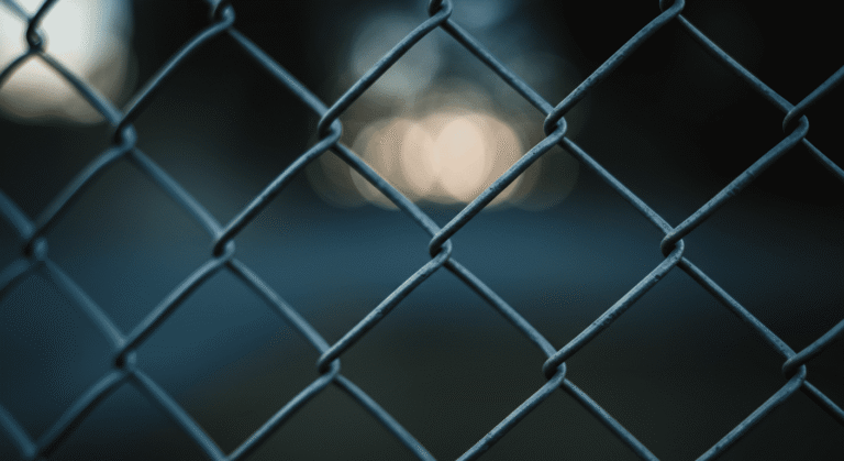 Primer plano de una valla de tela metálica con fondo desenfocado. Imagen con patrón de diamantes y bokeh suave ideal para fondos de pantalla y diseño gráfico.