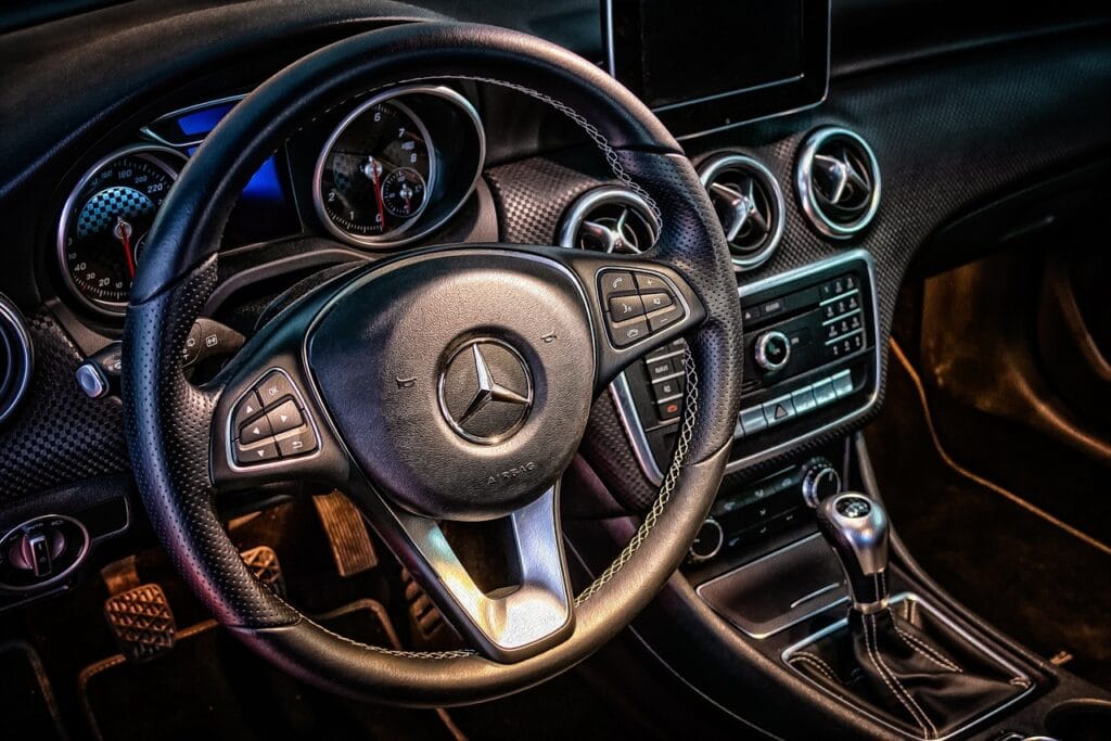 Interior de lujo de un coche Mercedes-Benz con volante de cuero, detalles modernos y consola central elegante.