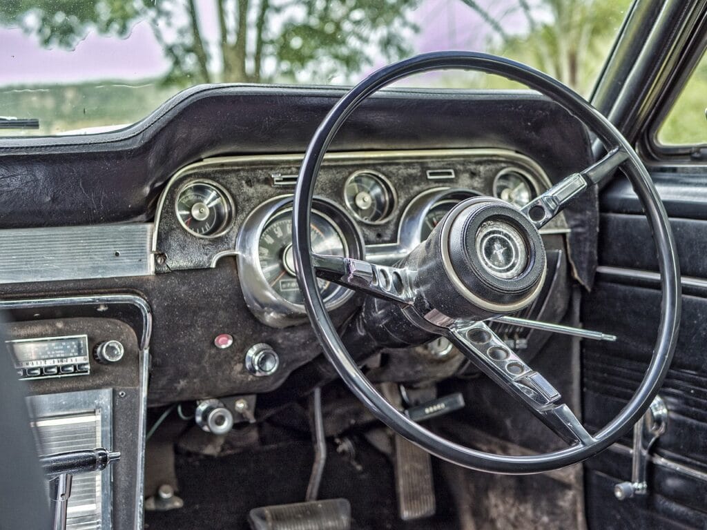 Interior de un automóvil vintage con volante grande y panel de instrumentos analógico, reflejando un diseño clásico.