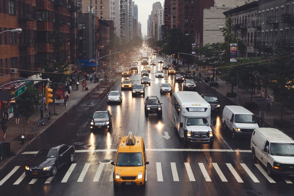 Tráfico urbano en una calle concurrida después de la lluvia, con taxis amarillos, autos y peatones en movimiento.