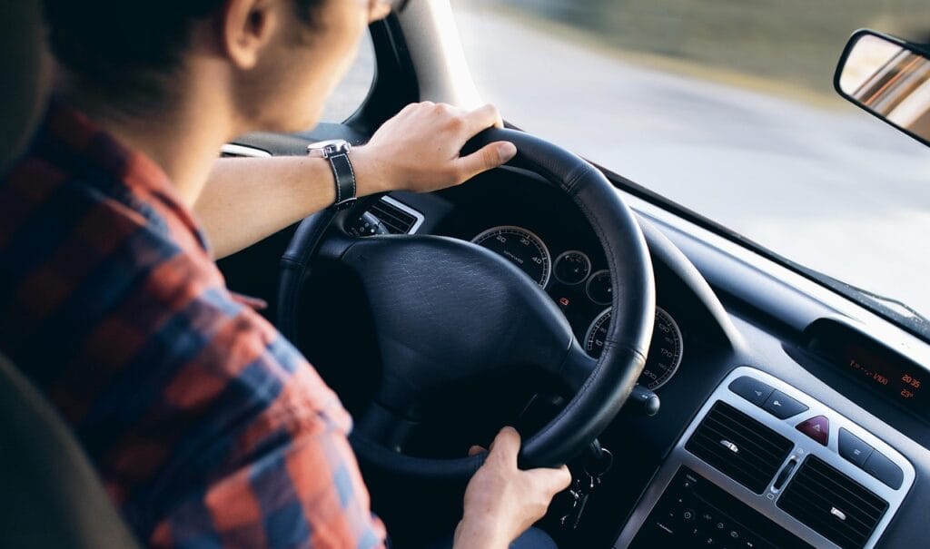 Hombre conduciendo un auto moderno con una vista clara del volante y el tablero en un día soleado.