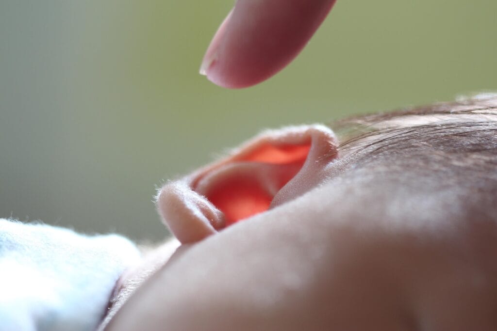 12 Cosas que le ocurren a tu cuerpo explicadas 4 Detalle de la oreja de un bebé con un dedo acercándose. Imagen de la delicada oreja de un niño pequeño a punto de ser tocada con un dedo.