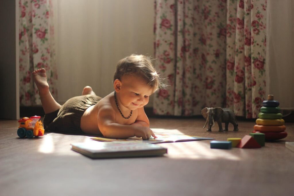 ¿Cómo percibe el mundo un bebé? 5 Bebé leyendo un libro en el suelo con juguetes. Imagen de un niño pequeño concentrado en la lectura, rodeado de juguetes como un tren y un elefante.