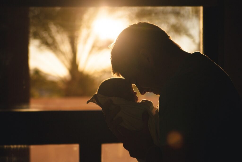¿Cómo percibe el mundo un bebé? 2 Silueta de padre con bebé al atardecer. Imagen de un padre sosteniendo a su hijo en brazos, con la luz del sol creando una silueta contra la ventana. Ideal para temas sobre paternidad, amor familiar y momentos especiales con bebés.