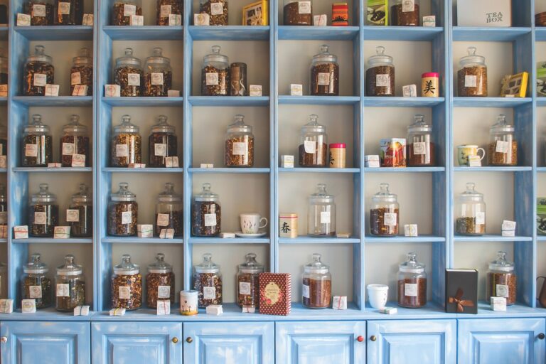 Moderna estantería de madera pintada de azul, organizada con frascos de vidrio llenos de hierbas y especias etiquetadas, ideal para una tienda de té o medicina natural.