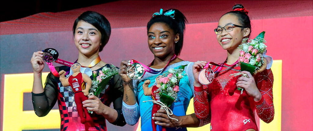 Historias inspiradoras: Atletas que convirtieron los obstáculos en triunfos 5 Tres gimnastas posan en un podio con sus medallas y ramos de flores, mostrando orgullo por sus logros en una competencia internacional.