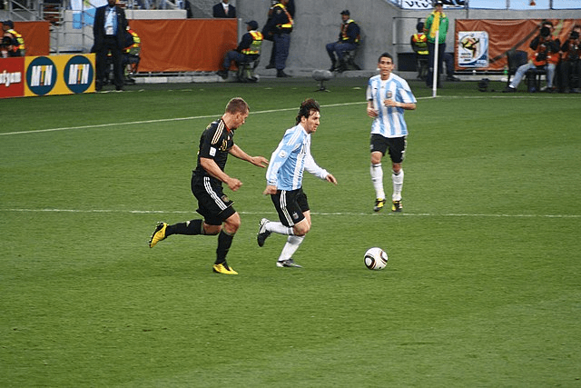 Historias inspiradoras: Atletas que convirtieron los obstáculos en triunfos 4 Lionel Messi jugando al fútbol con la selección Argentina, driblando el balón ante un defensor. Imagen de un partido de fútbol.