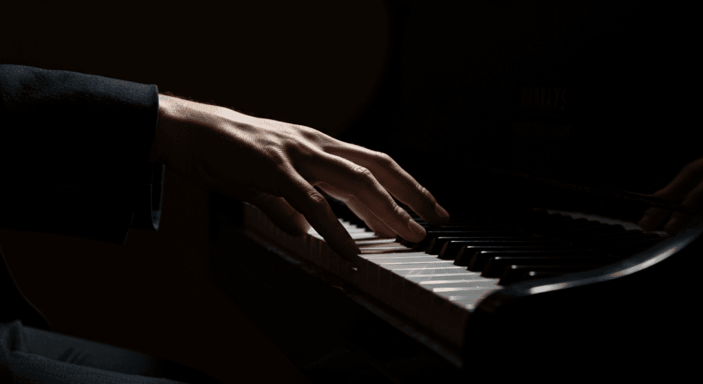 Los increíbles beneficios de tocar un instrumento musical 2 "Detalle de una mano tocando las teclas de un piano. Músico interpretando una pieza musical. Instrumento musical de teclado bajo una iluminación dramática."