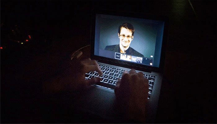 El caso Edward Snowden 4 Edward Snowden en videollamada desde un portátil en la oscuridad. Imagen de alguien tecleando con un portátil, con Snowden en pantalla. Conexión remota, privacidad digital y tecnología