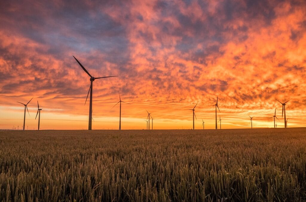 ¿Tiene Sentido el Cambio de Horario? Beneficios y Controversias 6 Campo de turbinas eólicas al atardecer, con un cielo colorido en tonos naranjas y púrpuras, simbolizando energía renovable y sostenibilidad.