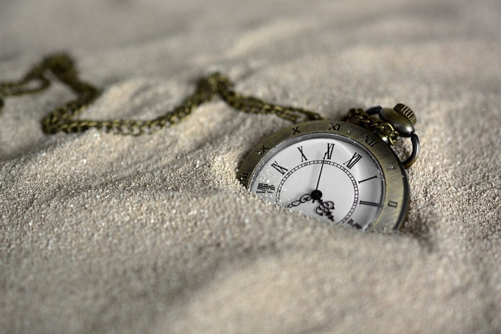 ¿Tiene Sentido el Cambio de Horario? Beneficios y Controversias 7 Reloj de bolsillo antiguo parcialmente enterrado en arena, con números romanos y cadena de metal. Representación del paso del tiempo y la nostalgia.