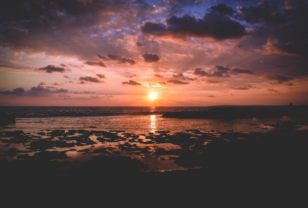 ¿Tiene Sentido el Cambio de Horario? Beneficios y Controversias 5 Atardecer sobre el océano con reflejos dorados en el agua y rocas en el primer plano. Escena tranquila y natural.