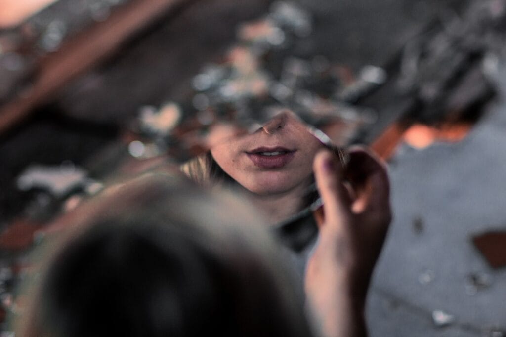El Peligro de la Falsa Autoestima: Cómo Detectarla y Fortalecer tu Confianza 7 Rostro femenino reflejado en un espejo fragmentado, mostrando labios y nariz en enfoque suave. Fondo oscuro con tonos cálidos.