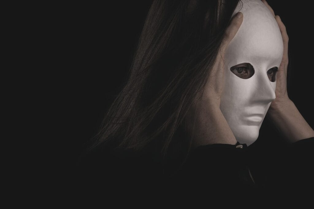 El Peligro de la Falsa Autoestima: Cómo Detectarla y Fortalecer tu Confianza 4 Persona sosteniendo una máscara blanca sin expresión contra su rostro, con fondo oscuro. Imagen dramática que representa temas de identidad y ocultamiento.