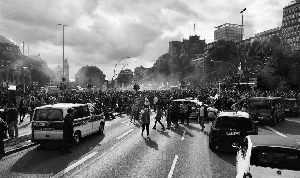 Pena de Muerte: Orígenes, Métodos y su Impacto en la Sociedad 5 Imagen en blanco y negro de una multitud en una protesta o manifestación, ocupando una calle urbana con vehículos policiales y edificios al fondo. Ambiente de tensión y movimiento.