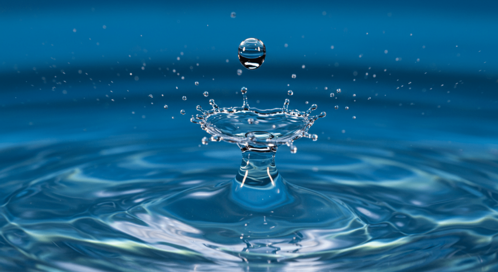 ¿Qué es la modernidad líquida? La teoría de un tiempo sin certezas 4 "Gota de agua macro: imagen de una gota suspendida sobre una superficie acuática azul con ondas. Ideal para contenido sobre fotografía macro, ciencia y naturaleza. Accesible para personas con discapacidad visual."