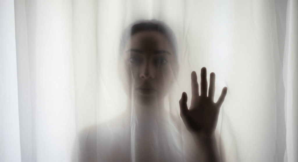 4 experiencias paranormales que te pondrán los pelos de punta 3 "Silueta tras cortina: imagen de una persona difuminada tras una cortina blanca, evocando misterio y vulnerabilidad. Ideal para contenido sobre emociones, privacidad y fotografía artística. Accesible para personas con discapacidad visual."