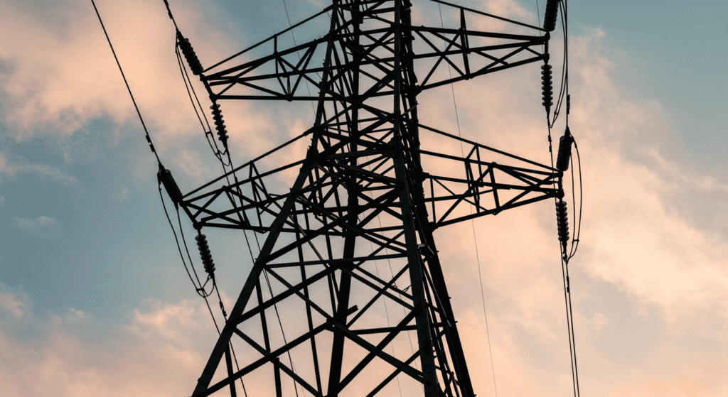 La Historia de la Electricidad: ¿Quiénes Fueron sus Inventores? 4 Torre de electricidad contra cielo con nubes rosadas. Energía, infraestructura.