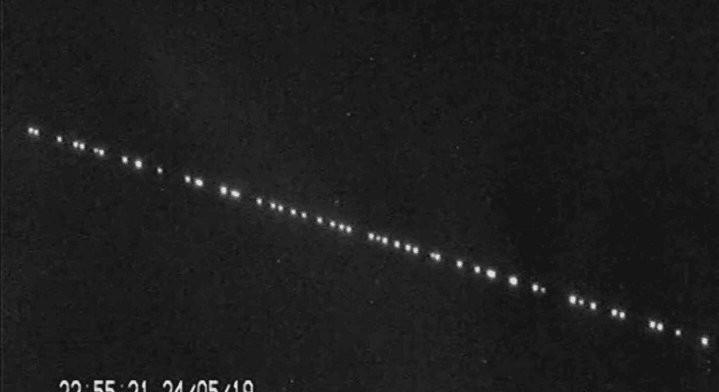 Imagen nocturna con una línea de puntos brillantes en el cielo. Posiblemente satélites Starlink.
